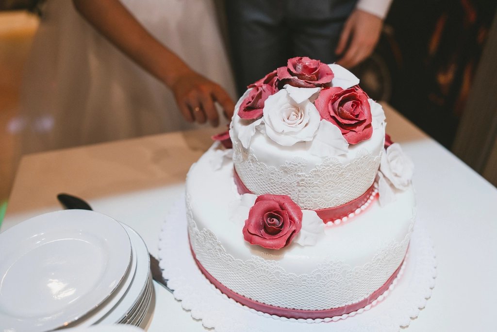 The cake table from a guest's seat — the bride reaching in, plates stacked and waiting.