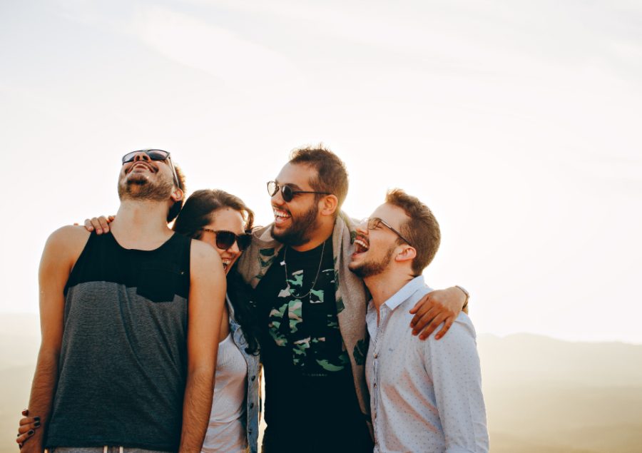 Four friends laughing arm in arm, caught off guard.
